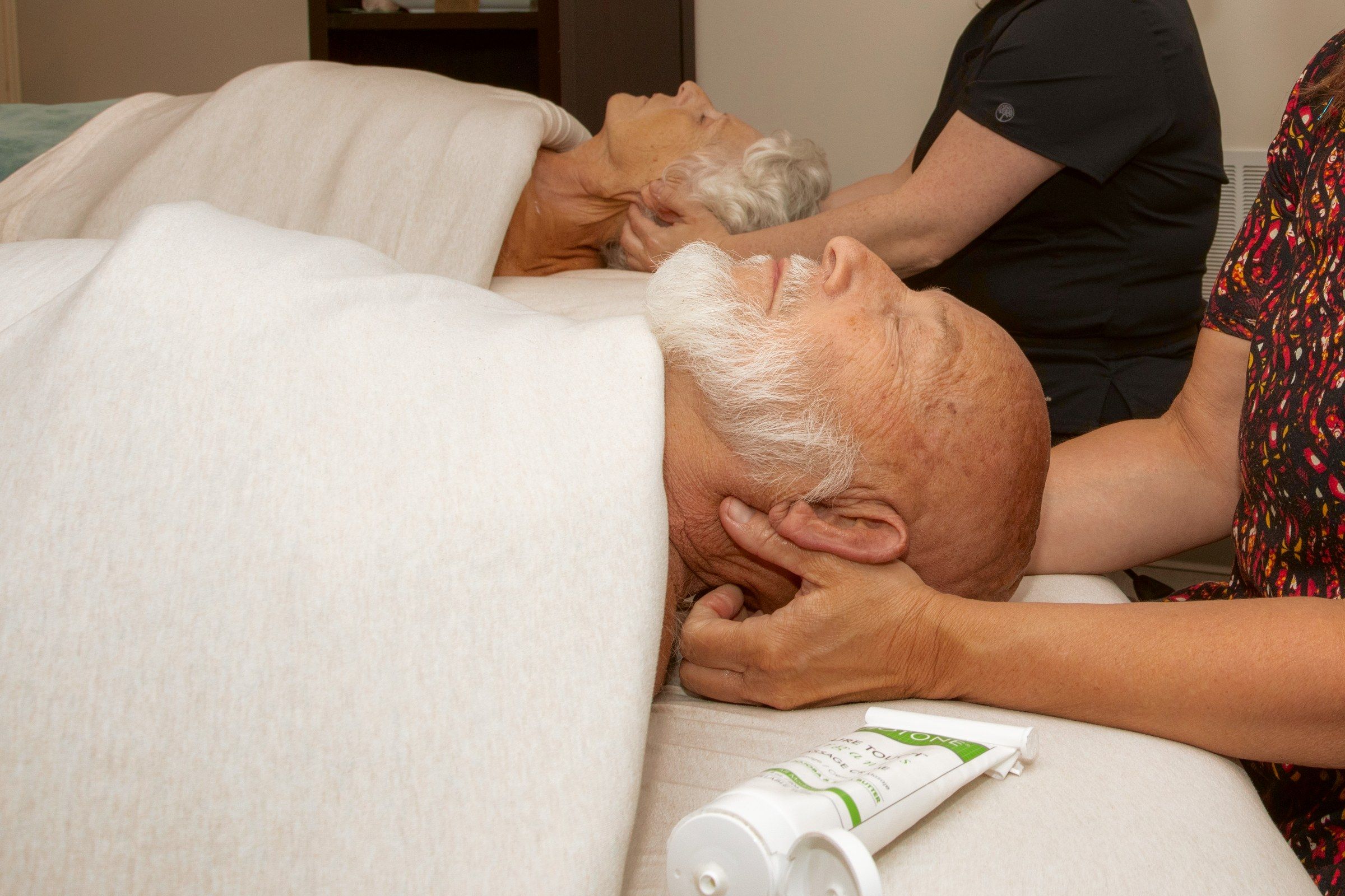 A couples session: a therapist working a client's face and neck, a second table beside