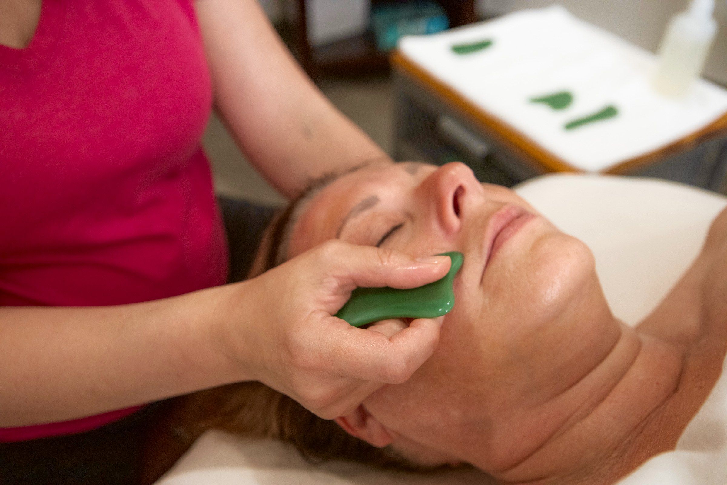 The gua sha stone gliding along a client's cheek
