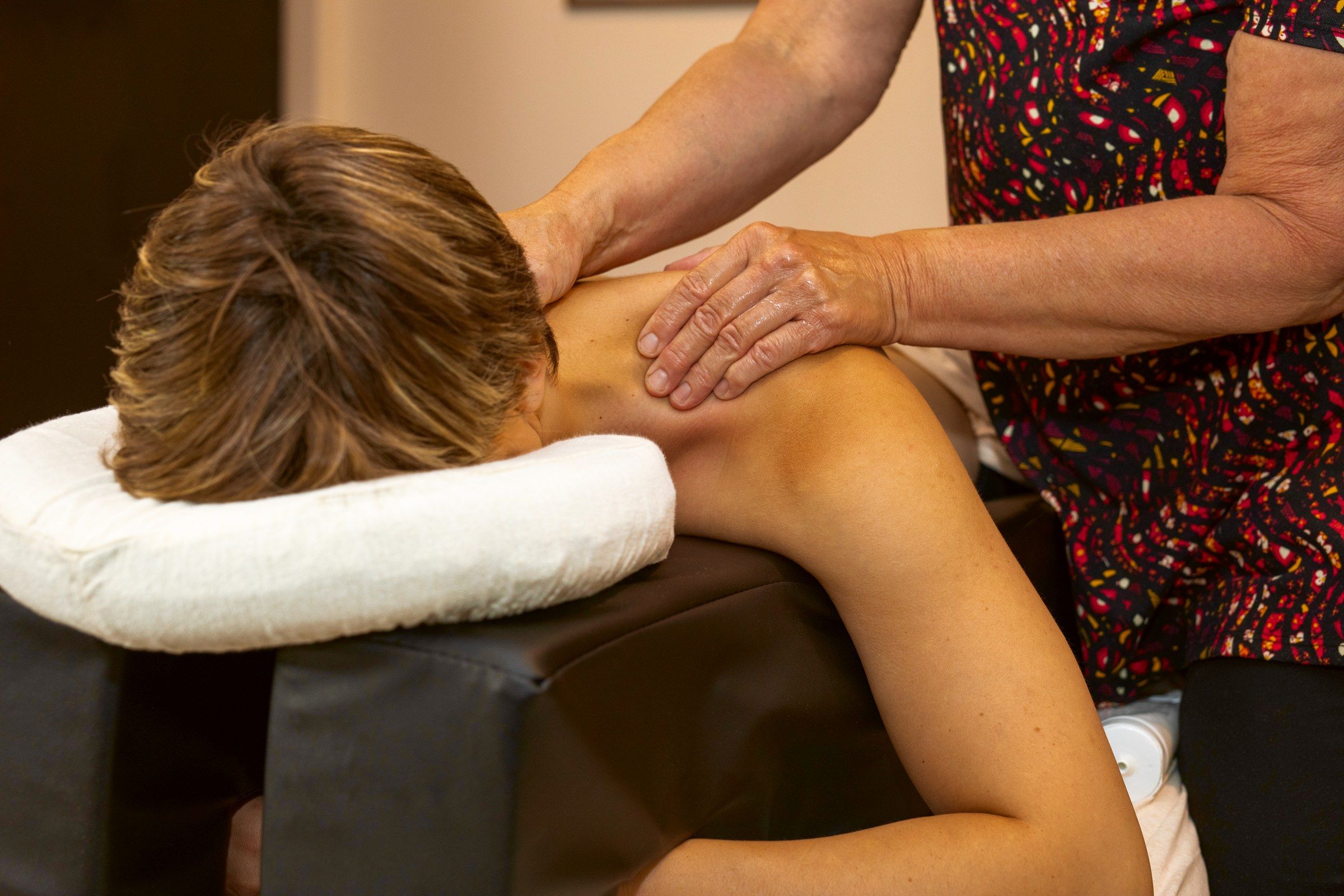 Hands working the shoulders of a client resting on a pregnancy cushion