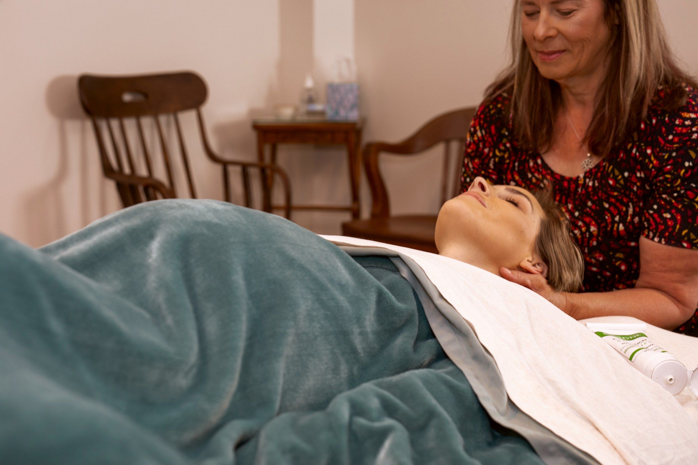 A pregnant client resting face up under a blanket while her therapist works her neck and shoulders